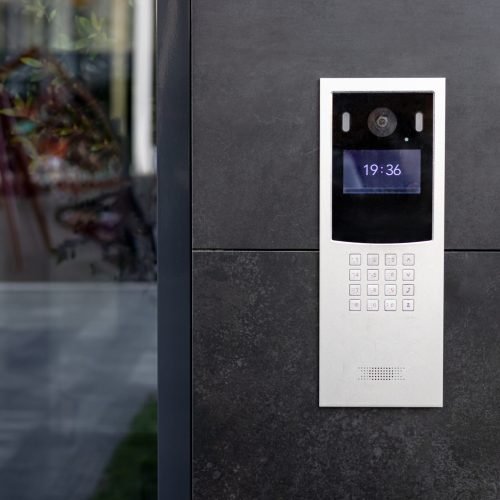 Entrance doorbell in a multi-apartment building, with a video surveillance camera, on a dark wall.