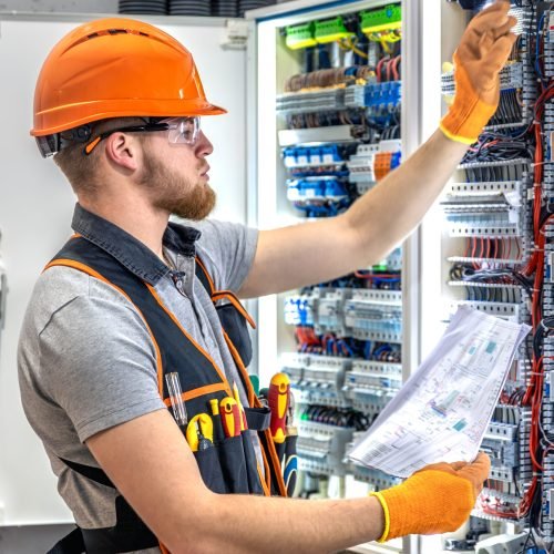 Male electrician working in electrical panel. Male electrician in uniform. High quality photo. Male construction worker in helmet and safety glasses.